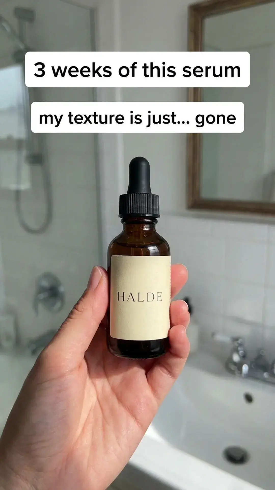 Vertical UGC video poster for Halde serum: a hand holding the amber bottle in a tiled bathroom, captions “3 weeks of this serum” and “my texture is just… gone”.